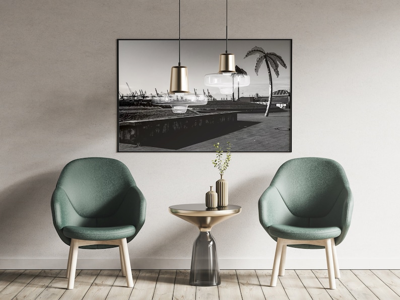 May include: Two green chairs with wooden legs and a glass and gold side table in front of a black and white photograph of a palm tree and a cityscape.