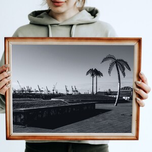 May include: A framed black and white photograph of a harbor scene with palm trees in the foreground. The harbor has several cranes and buildings in the background.