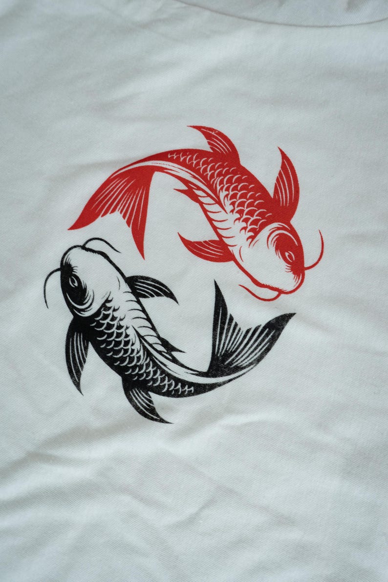 K&ouml;nnte beinhalten: Wei&szlig;er Stoff mit einem Design aus roten und schwarzen Koi-Fischen. Die Fische sind kreisf&ouml;rmig angeordnet, wobei sich ein roter und ein schwarzer Fisch gegen&uuml;berstehen. Das Design ist eine einfache, grafische Illustration.
