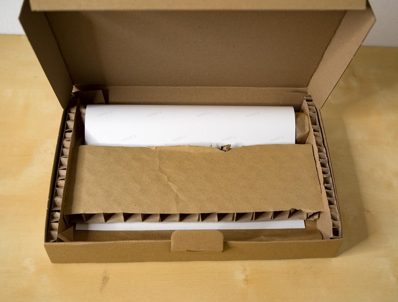 May include: A brown cardboard box with its lid open, revealing a white rolled-up item inside. The box is filled with brown packing peanuts for protection.