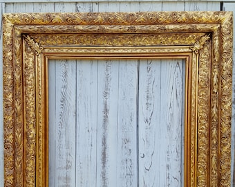 Puede incluir: Un marco de imagen grande y dorado adornado con tallas intrincadas. El marco está hecho de madera y tiene un acabado desgastado.