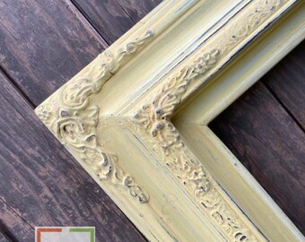 May include: A yellow picture frame with ornate detailing and a distressed finish. The frame is made of wood and has a light yellow color with a hint of blue.