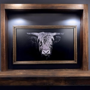 Puede incluir: Una pieza de arte mural enmarcada de forma rectangular que presenta un retrato en blanco y negro de alto contraste de una vaca Highland con pelaje largo y desgre&ntilde;ado y cuernos prominentes, dentro de un marco de madera oscura.