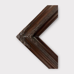 May include: A section of a dark brown picture frame with ornate detailing. The frame has a beveled edge and decorative corner accents. The wood grain is visible, adding texture to the classic design.