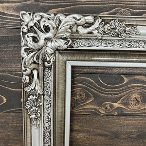 May include: A silver ornate picture frame with a detailed floral design. The frame is made of wood and has a distressed finish.