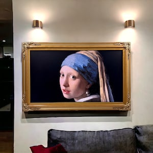 May include: A framed reproduction of the painting Girl with a Pearl Earring, featuring a person wearing a blue headscarf and a large pearl earring against a dark background, encased in an ornate, rectangular gold-colored decorative frame.