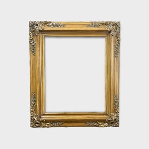May include: A gold-colored ornate picture frame with a decorative, carved design. The frame is empty and ready to display a photo or artwork.