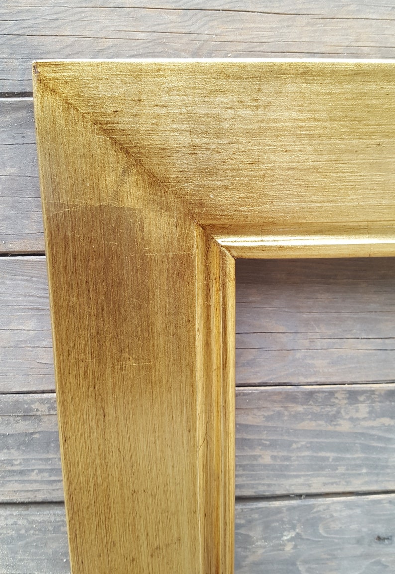 Peut inclure: Gros plan sur un cadre photo en bois peint en or avec une finition l&eacute;g&egrave;rement vieillie. Le cadre a un design simple et classique avec un bord sur&eacute;lev&eacute;.