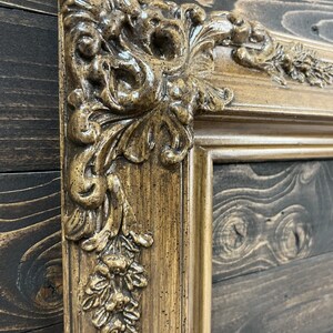 May include: A close-up of a decorative, ornate picture frame with a gold and brown finish. The frame has a detailed, carved design with a textured surface.