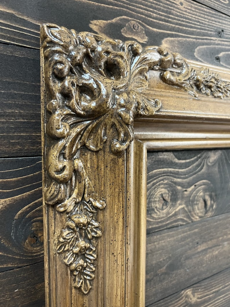 May include: A close-up of a decorative, ornate picture frame with a gold and brown finish. The frame has a detailed, carved design with a textured surface.