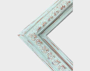 May include: Close-up of a corner of a distressed, ornate picture frame. The frame is painted a light turquoise color with visible brown undertones and decorative relief details. The frame's design is classic and vintage.