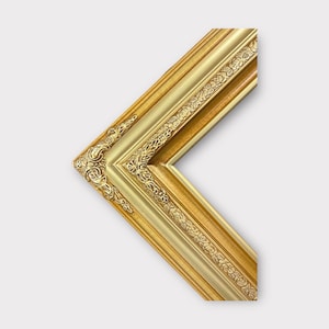 May include: A gold picture frame with ornate detailing. The frame has a raised edge and a decorative pattern around the outer edge.