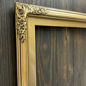 May include: A gold picture frame with ornate detailing around the edges. The frame is made of wood and has a distressed finish.