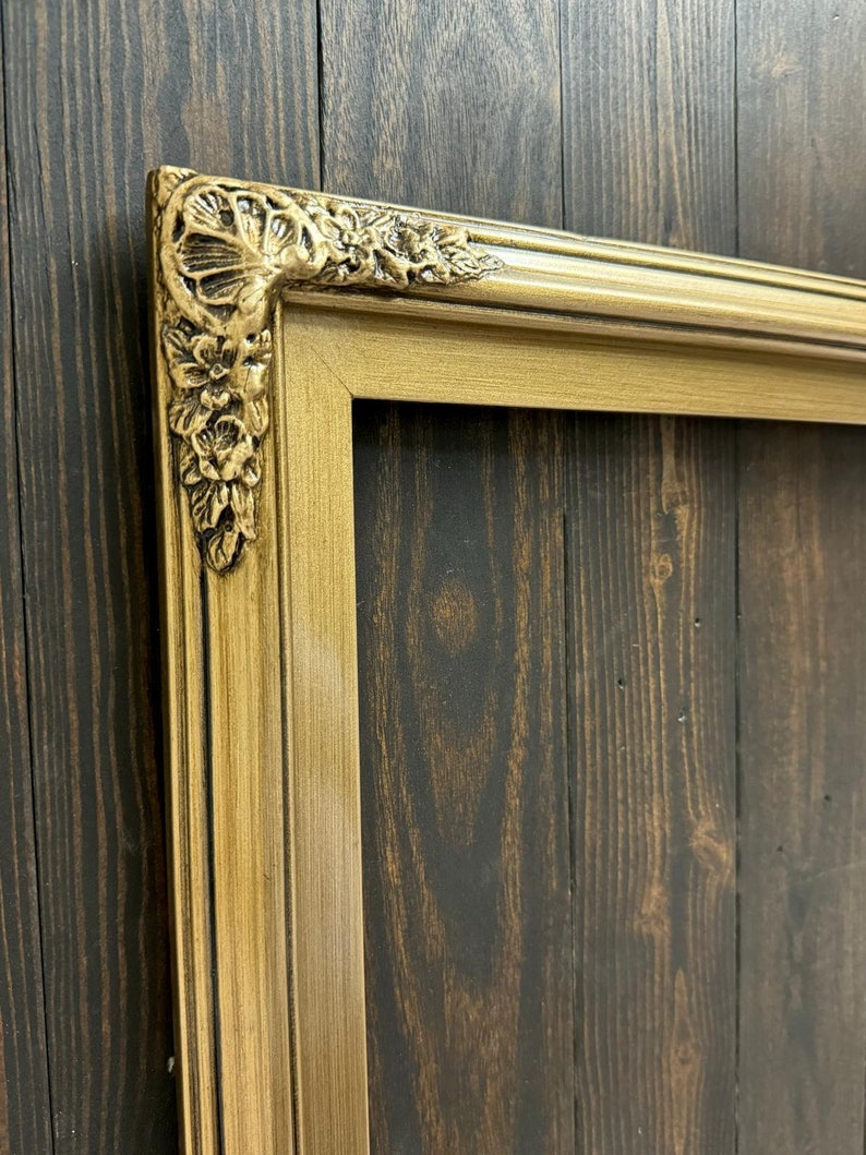 May include: A gold picture frame with ornate detailing around the edges. The frame is made of wood and has a distressed finish.