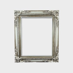 May include: A silver ornate picture frame with a decorative, detailed design. The frame is empty and ready to display a photo or artwork.