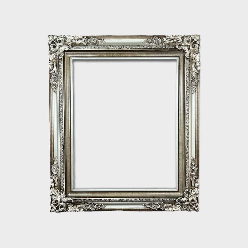 May include: A silver ornate picture frame with a decorative, detailed design. The frame is empty and ready to display a photo or artwork.
