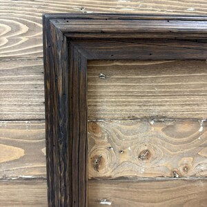 Puede incluir: Un marco rectangular construido con madera oscura y desgastada con un patr&oacute;n de veta visible. El marco presenta una uni&oacute;n en inglete y un dise&ntilde;o de perfil escalonado de varios niveles con un acabado profundo y peque&ntilde;as hendiduras.