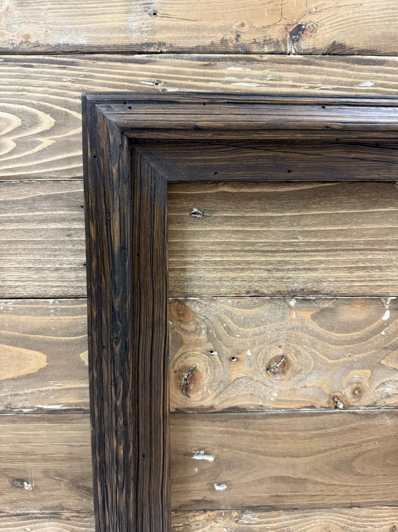Puede incluir: Un marco rectangular construido con madera oscura y desgastada con un patr&oacute;n de veta visible. El marco presenta una uni&oacute;n en inglete y un dise&ntilde;o de perfil escalonado de varios niveles con un acabado profundo y peque&ntilde;as hendiduras.