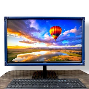 May include: A computer monitor with a dark blue ornate frame displaying a vibrant image of a colorful hot air balloon floating over a lake at sunset. The Acer logo is visible on the bottom bezel, and a black computer keyboard sits in front.