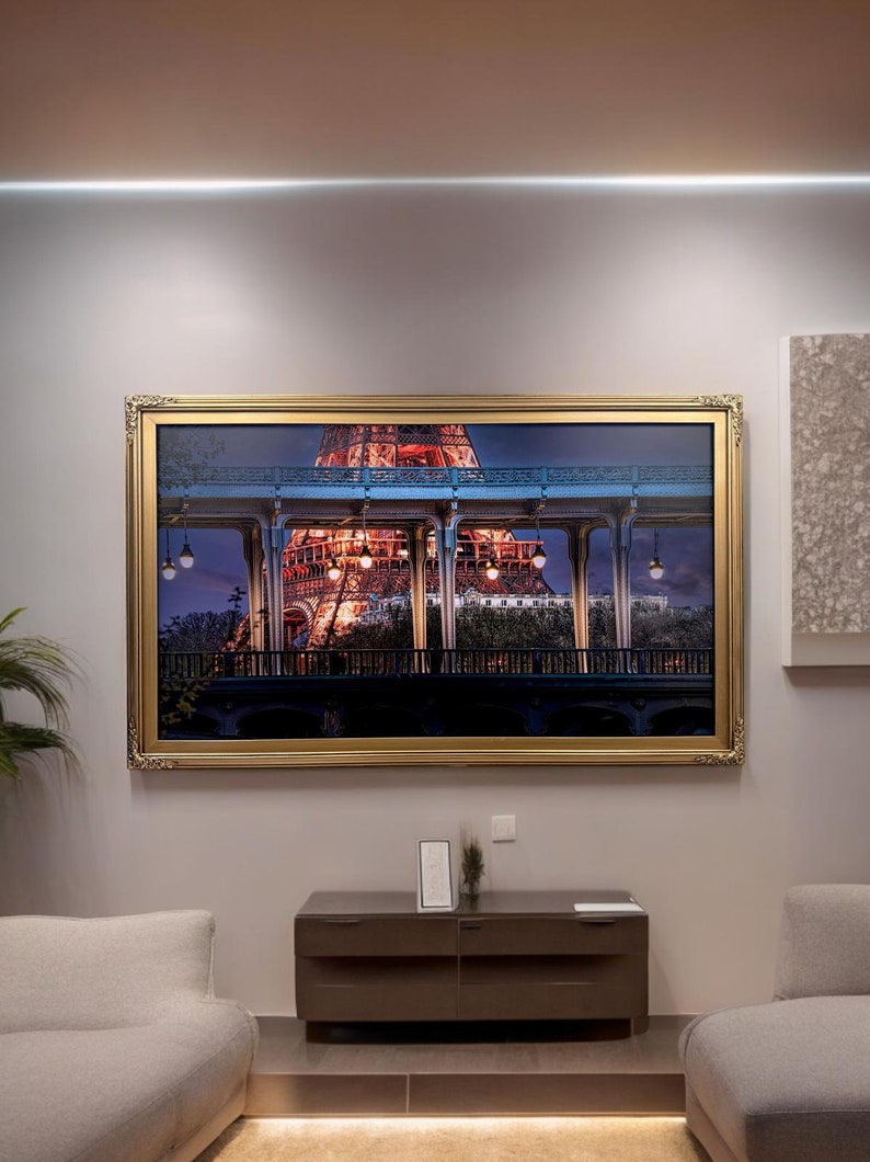 May include: A framed photograph of the Eiffel Tower at night, with the lights of the city in the background. The photo is in a gold frame and is hanging on a wall.