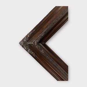 May include: A dark brown wooden picture frame with ornate detailing. The frame has a beveled edge and a slightly raised lip.