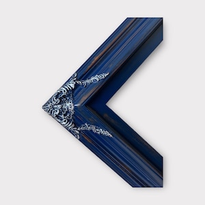 May include: A dark blue picture frame with ornate, white, decorative details on the corners. The frame is made of wood and has a distressed finish.