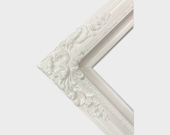 May include: White ornate picture frame with a detailed, raised, floral design. The frame is made of wood and has a smooth, painted finish.
