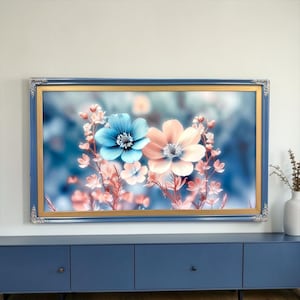 May include: A rectangular wall art piece featuring a floral illustration with one prominent blue flower and one prominent peach flower, surrounded by smaller blossoms on thin stems. The artwork is encased in a blue frame with gold trim.