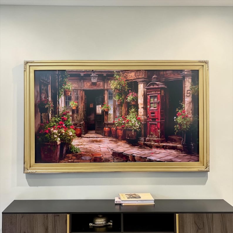 May include: A rectangular framed painting depicting a cobblestone courtyard with a red telephone booth, numerous potted plants with red and green foliage, and architectural details including a doorway marked with the number five.