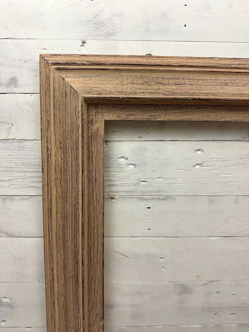 May include: A rectangular picture frame featuring a light brown wood finish with a visible grain texture and dark distressed accents. The frame has a multi-tiered stepped profile with clean mitered corners, showcasing a natural weathered appearance.