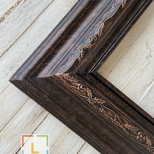 May include: A dark brown picture frame with a decorative, ornate, copper-colored design. The frame has a distressed look and is made of wood.