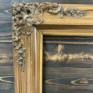 May include: A close-up of a brown ornate picture frame with a detailed, carved design. The frame is made of wood and has a distressed finish.