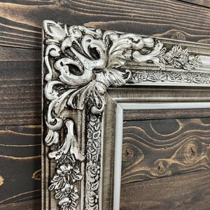 May include: A silver ornate picture frame with a detailed floral design. The frame is made of wood and has a distressed finish.