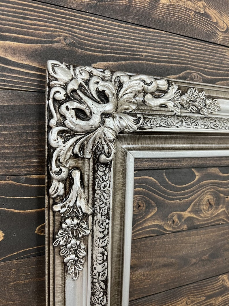 May include: A silver ornate picture frame with a detailed floral design. The frame is made of wood and has a distressed finish.