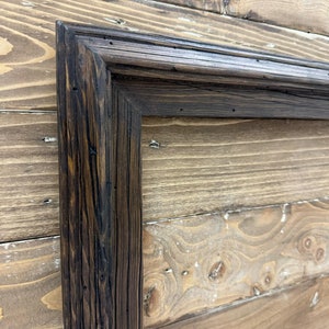 Puede incluir: Un marco rectangular hecho de madera oscura y desgastada con una veta visible y una superficie texturizada. El marco presenta esquinas en inglete y un acabado te&ntilde;ido profundo que resalta las imperfecciones naturales y las vetas de la madera.