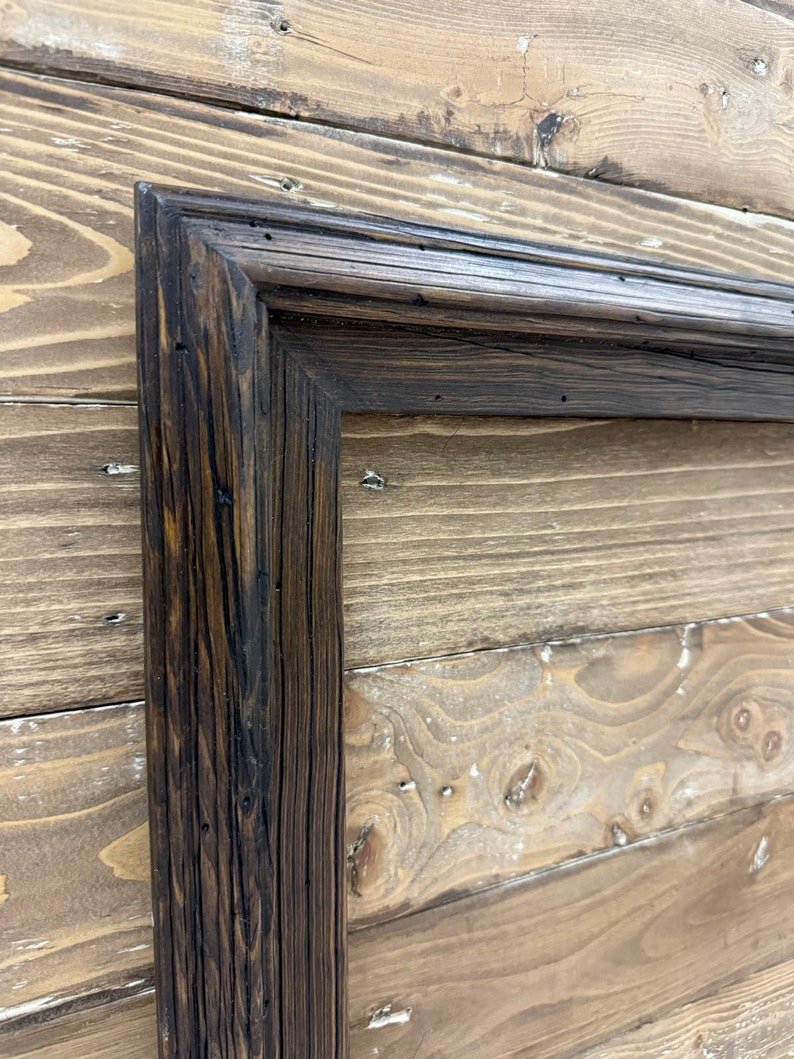 Puede incluir: Un marco rectangular hecho de madera oscura y desgastada con una veta visible y una superficie texturizada. El marco presenta esquinas en inglete y un acabado te&ntilde;ido profundo que resalta las imperfecciones naturales y las vetas de la madera.