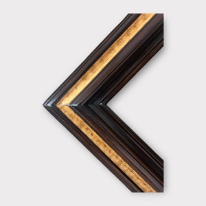 May include: A corner of a dark brown picture frame with a gold accent. The frame has a beveled edge and a glossy finish. The gold accent runs along the inner edge of the frame.