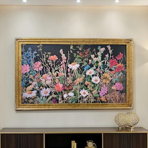 May include: A rectangular wall painting featuring a vibrant meadow of wildflowers in shades of pink, white, blue, and orange against a dark black background, accented by two orange butterflies, all enclosed within a textured gold-toned frame.