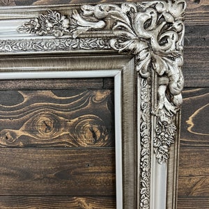 May include: A silver ornate picture frame with a white inner border. The frame has a detailed floral design and is made of wood.