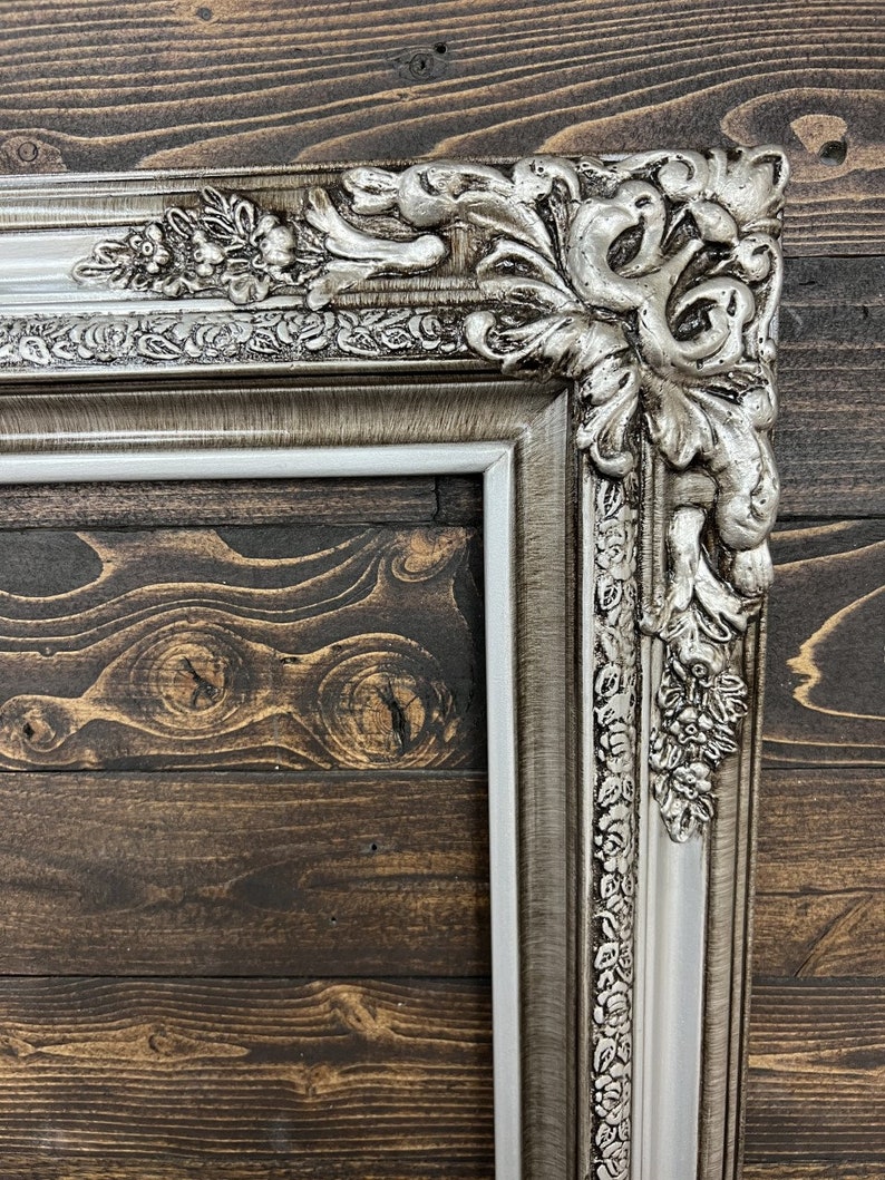 May include: A silver ornate picture frame with a white inner border. The frame has a detailed floral design and is made of wood.