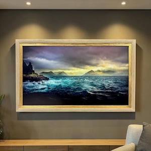 May include: A rectangular landscape painting in a light-colored wooden frame with a gold inner border. The artwork depicts a dark, turbulent ocean with deep blue waves crashing against a rocky cliffside under a dramatic, cloudy sky.