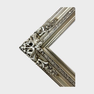 May include: A silver picture frame with ornate detailing around the edges. The frame is made of wood and has a distressed finish.
