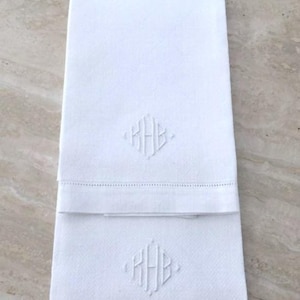 Könnte beinhalten: Zwei weiße Handtücher mit gestickten Initialen "HHB" in einer Diamantform.