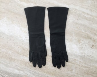 May include: A pair of long black leather gloves. The gloves are fully extended and laid flat on a light beige surface.