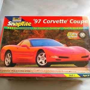 May include: A model kit box for a '97 Corvette Coupe. The box features a vibrant image of the red sports car. The Revell SnapTite kit includes peel and stick decals and requires no gluing or painting. The scale is 1:25.