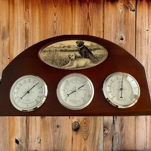 Puede incluir: Estación meteorológica de madera con tres medidores y una ilustración de perro en tonos sepia. Los medidores muestran lecturas de termómetro, barómetro y humedad. El termómetro está en Fahrenheit.
