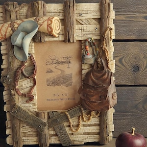 May include: A rustic polyresin photo frame with a weathered wood design, adorned with miniature cowboy-themed embellishments. The frame holds a 8.9cm x 12.7cm image and features a small backpack and a red apple.