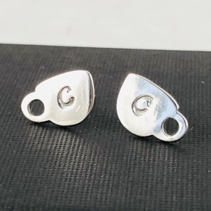 May include: A pair of silver earrings shaped like coffee cups with the letter "C" engraved on each cup.