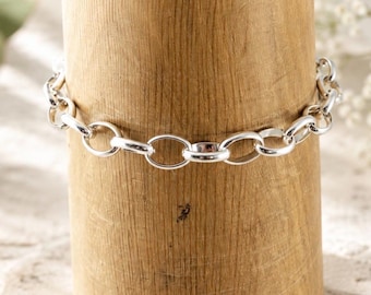 Puede incluir: Una pulsera de cadena plateada con eslabones ovalados redondeados y pulidos, conectados en un bucle continuo. El metal tiene un acabado brillante y reflectante que capta la luz, creando una apariencia suave y uniforme a lo largo de toda la cadena.