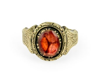 May include: A gold ring with an ornate design and a red gemstone.